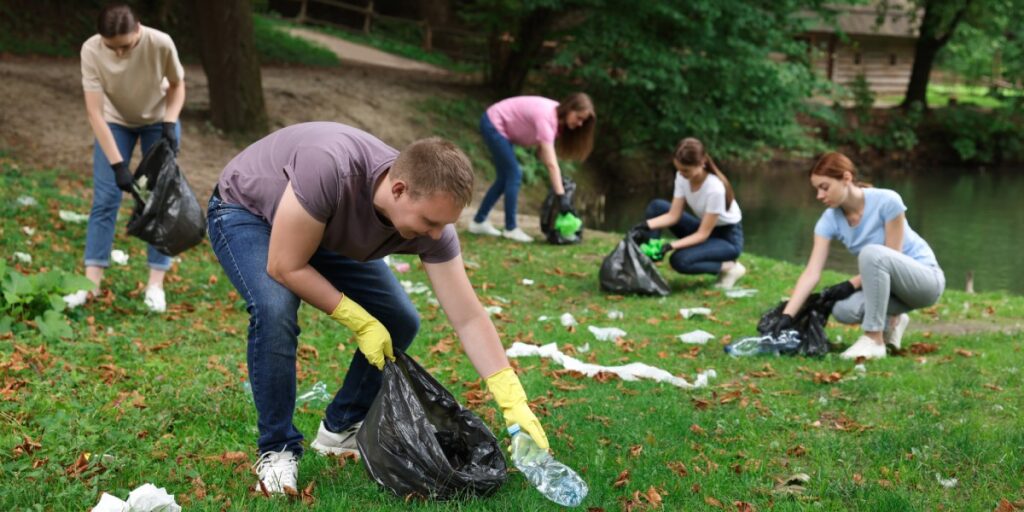 A group of friends cleaning up their local park. They all have plastic trash bags and gloves to collect garbage.