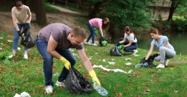 A group of friends cleaning up their local park. They all have plastic trash bags and gloves to collect garbage.