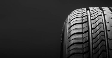 A close-up profile of a summer performance automotive tire and its tread design against a black background.