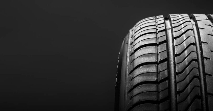 A close-up profile of a summer performance automotive tire and its tread design against a black background.