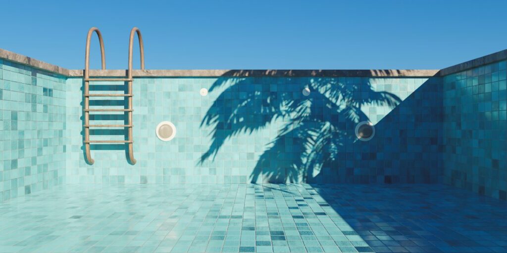 An empty swimming pool with turquoise tiles, a small step ladder, and the shadow of a palm tree on a beautiful, clear day.