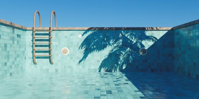 An empty swimming pool with turquoise tiles, a small step ladder, and the shadow of a palm tree on a beautiful, clear day.