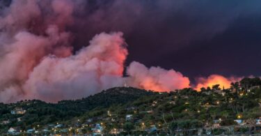 A wildfire engulfing a beach city and filling the air with smoke, smog, ash, and flame, destroying homes.