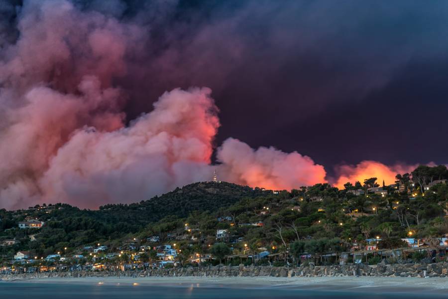 A wildfire engulfing a beach city and filling the air with smoke, smog, ash, and flame, destroying homes.