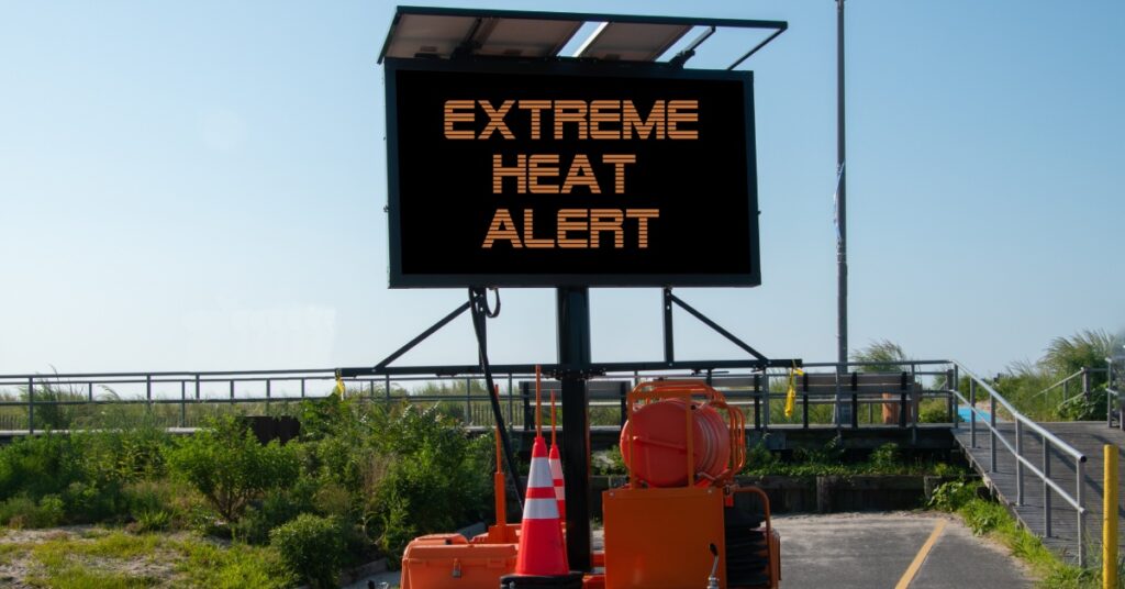 An electronic construction sign on the side of a concrete path leading up to a boardwalk that reads "EXTREME HEAT ALERT".