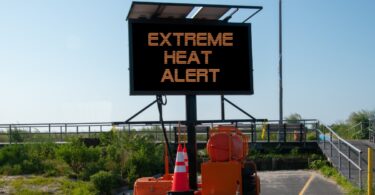 An electronic construction sign on the side of a concrete path leading up to a boardwalk that reads "EXTREME HEAT ALERT".