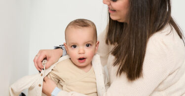 A young mother helps get her newborn dressed for the day as she places a comfortable jacket on her baby.