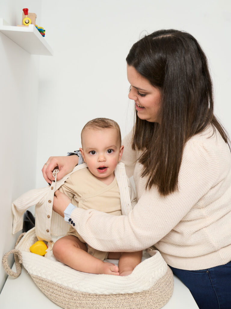 A young mother helps get her newborn dressed for the day as she places a comfortable jacket on her baby.