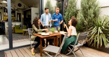 A diverse group of young adults having fun and laughing in the backyard, while drinking and eating small plates.