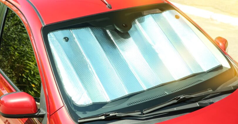 A top view of a red commuter vehicle with a sunshade set up in the windshield on a hot, sunny day.