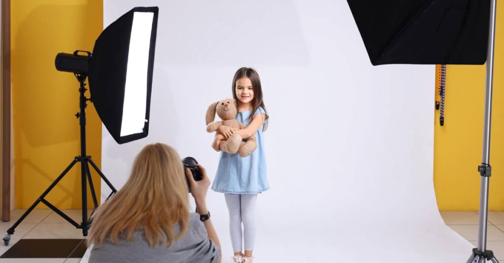 A girl posing for a picture while in a professional photography studio. The photographer is kneeling in the foreground.