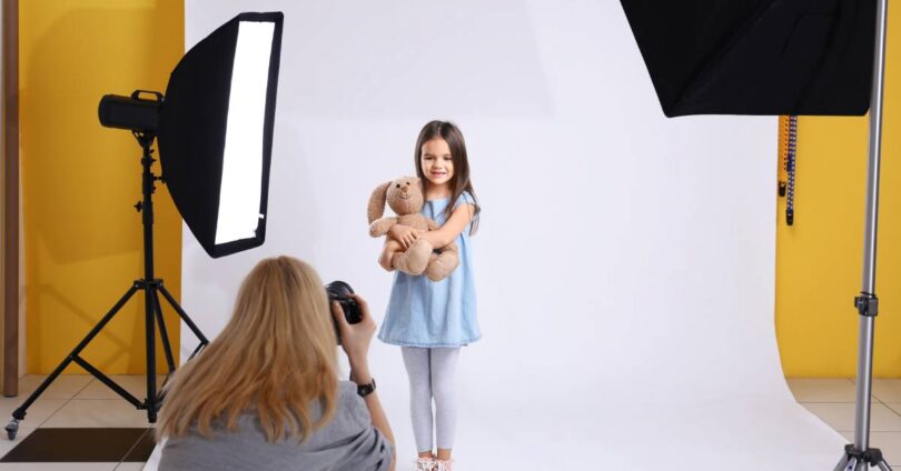 A girl posing for a picture while in a professional photography studio. The photographer is kneeling in the foreground.