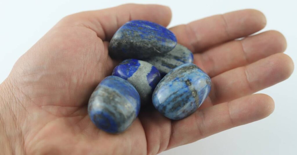 Someone holding a small collection of lapis lazuli stones. Each stone has striations and variations running through the blue.