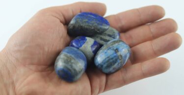 Someone holding a small collection of lapis lazuli stones. Each stone has striations and variations running through the blue.