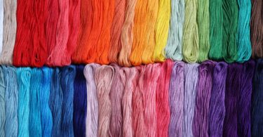 A vibrant rainbow of embroidery threads in various shades. The bundles of thread are placed next to each other in two rows.