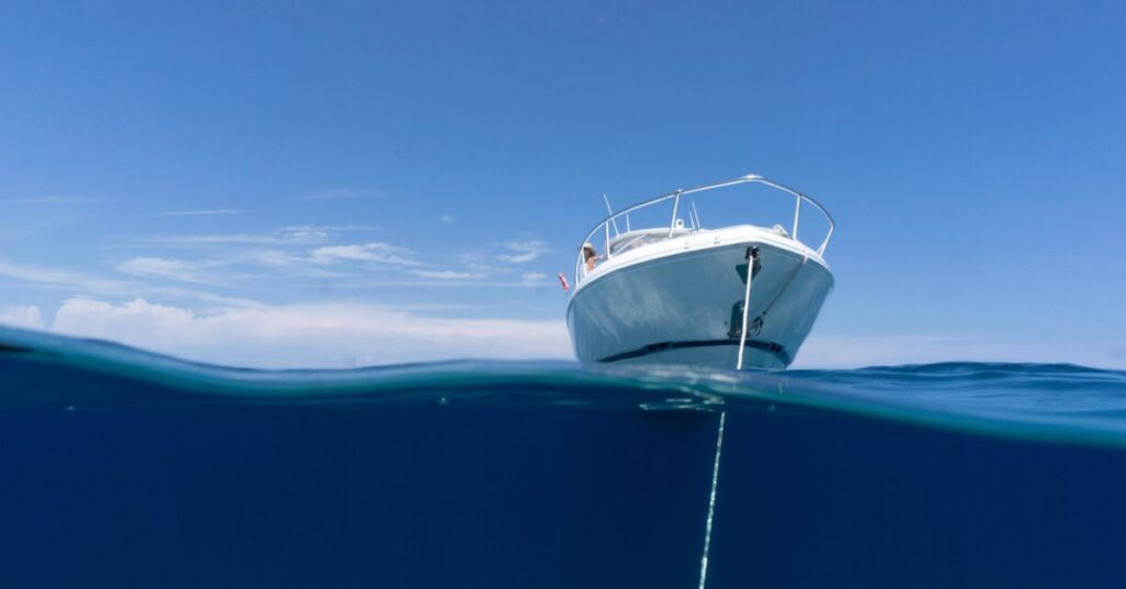 A boat on the water with the anchor dropped in and the boat sitting still. The sky and water are a pretty blue.
