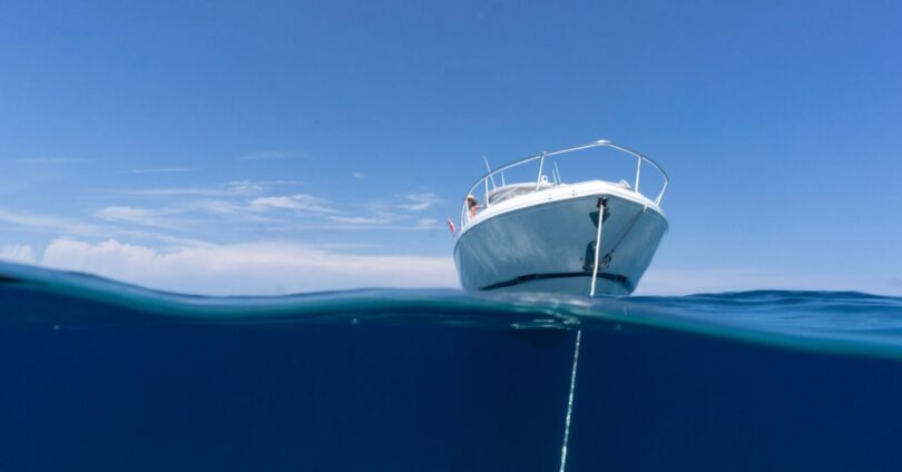 A boat on the water with the anchor dropped in and the boat sitting still. The sky and water are a pretty blue.