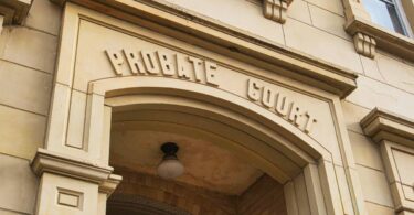 The exterior of probate court house with brown stone architecture and a lamp on the ceiling in the entryway.