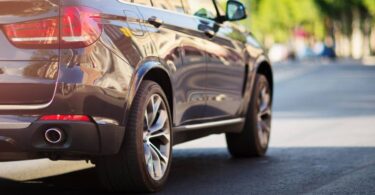 The back of a luxury SUV driving down the road on a sunny day. The vehicle is gray and has new tires.