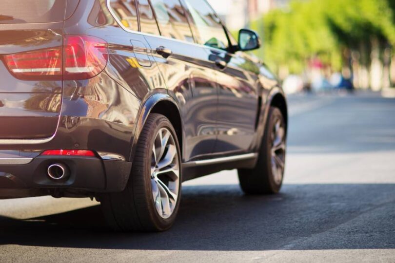 The back of a luxury SUV driving down the road on a sunny day. The vehicle is gray and has new tires.