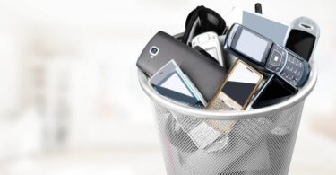 A collection of old cell phones and devices in a small metal trash bin. The phones are from early 2000s.