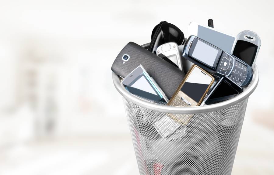 A collection of old cell phones and devices in a small metal trash bin. The phones are from early 2000s.
