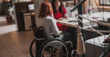Two women sit at a restaurant table. One woman is a wheelchair user and sits at the end of the table.