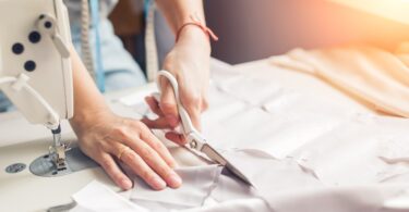 A woman carefully uses her cutting skills—one of her sewing abilities—while working with fabric and a sewing machine.