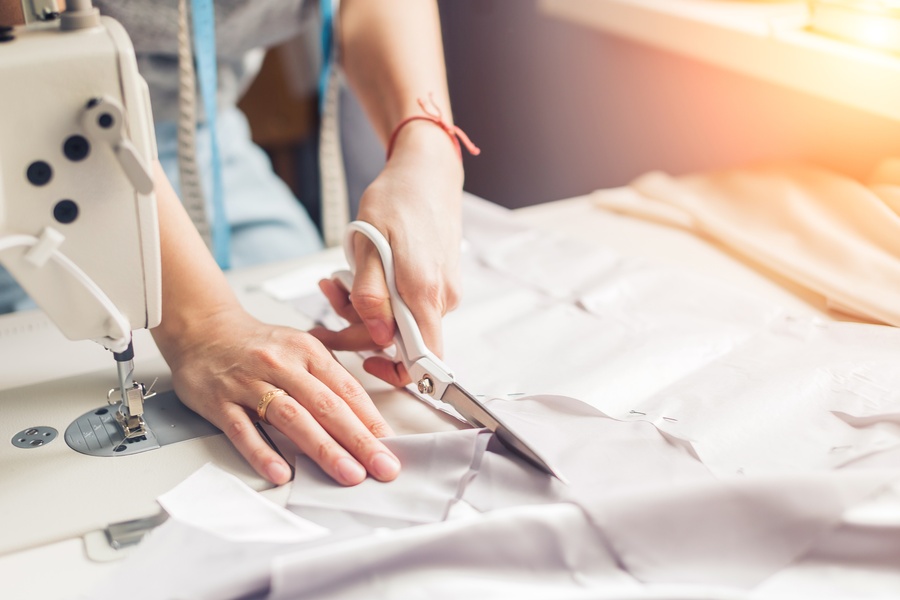 A woman carefully uses her cutting skills—one of her sewing abilities—while working with fabric and a sewing machine.