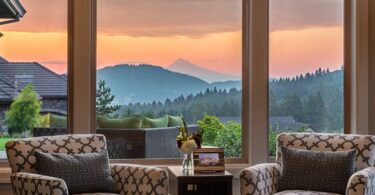 A beautiful view of the mountains shown through a home's large picture window. There's two chairs near the window.