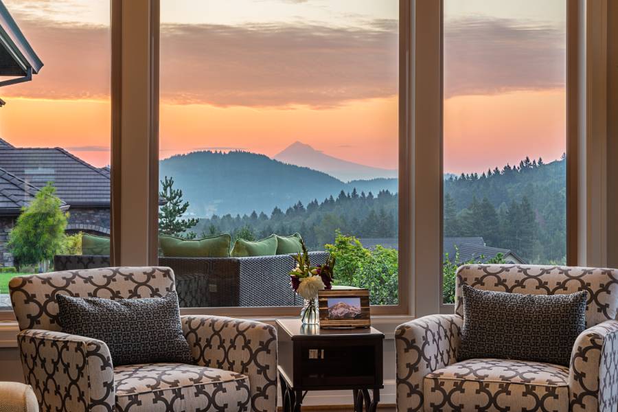 A beautiful view of the mountains shown through a home's large picture window. There's two chairs near the window.