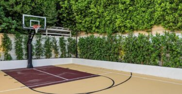 An outdoor community sport court tucked into a tree line. The court features a full basketball court and court lines.