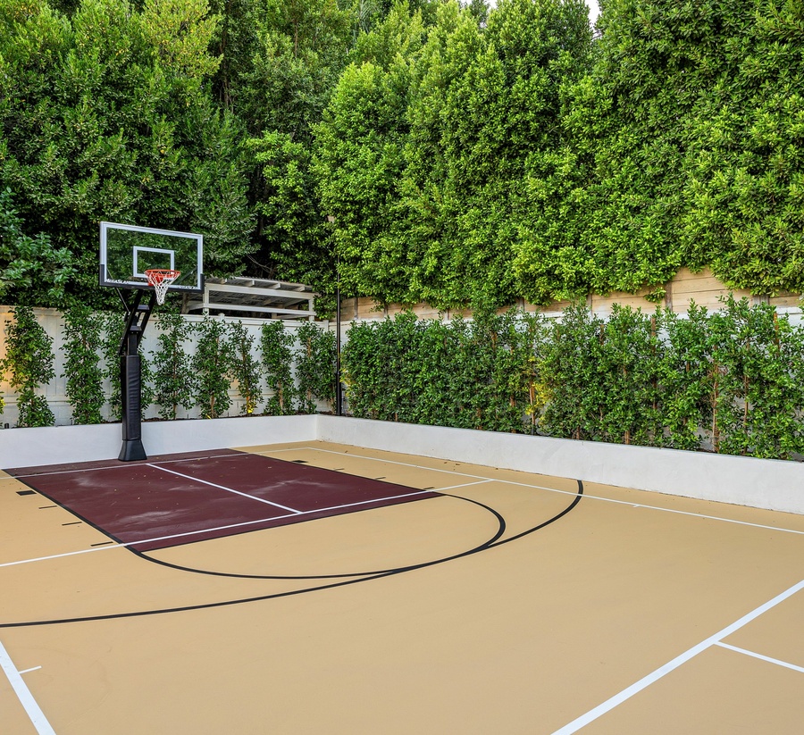 An outdoor community sport court tucked into a tree line. The court features a full basketball court and court lines.