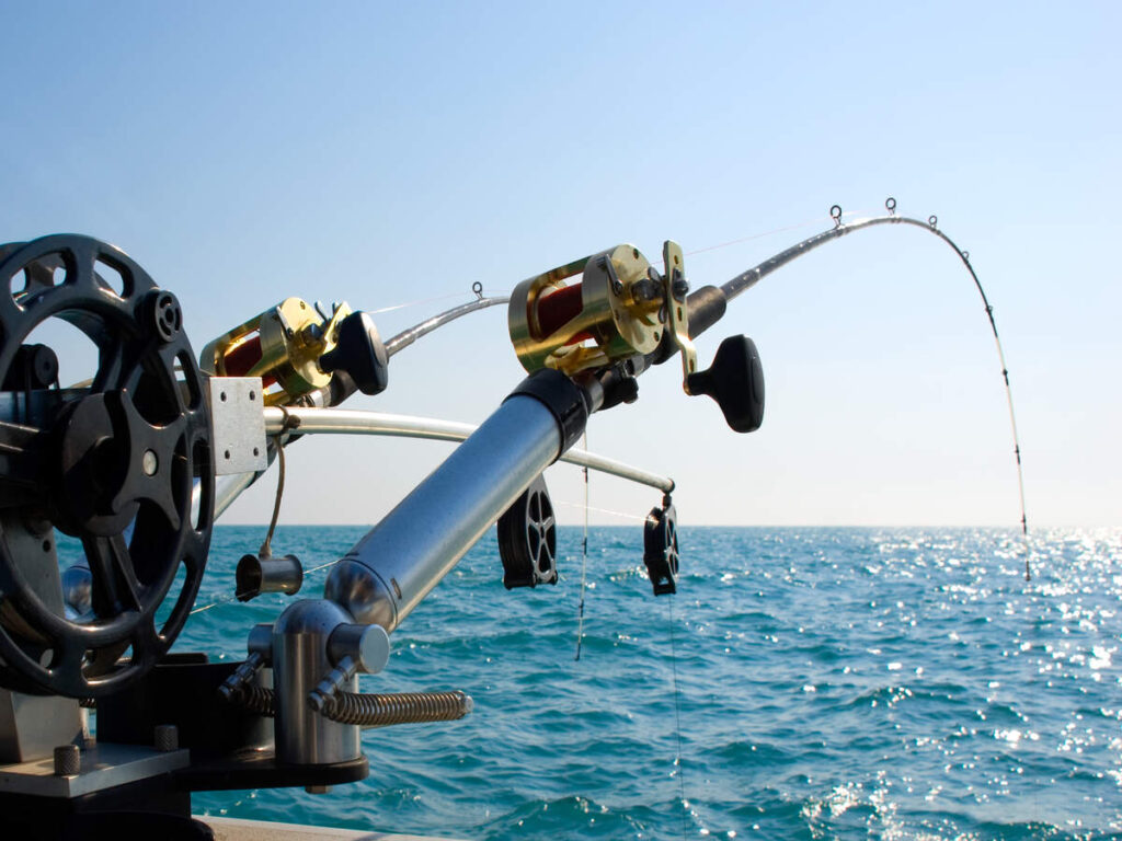 A close-up of two fishing rods on the back of a vessel. Clear blue water is in the background, with no shore in sight.