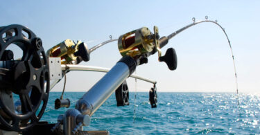 A close-up of two fishing rods on the back of a vessel. Clear blue water is in the background, with no shore in sight.