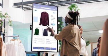 A person in a tan shirt is using a large touchscreen display that contains a shirt design in different colors.