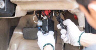 A mechanic with white work gloves on as they work on automotive wiring tasks under a car's steering column.