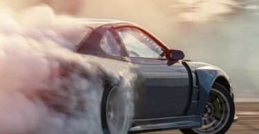 A sporty vehicle making a sharp turn on a drag racing track. Smoke billows out from behind the back tire.