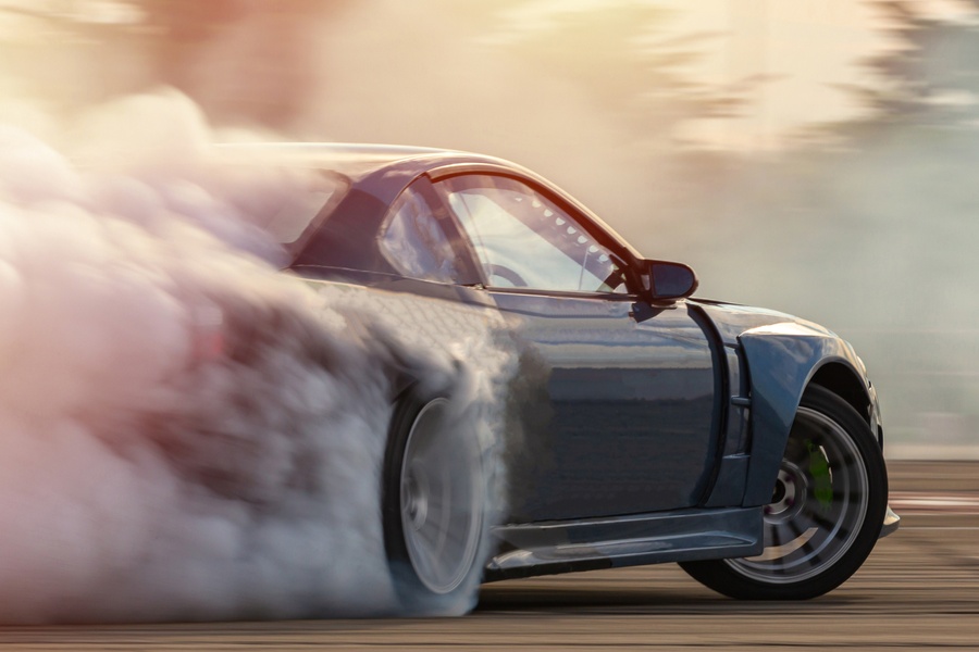 A sporty vehicle making a sharp turn on a drag racing track. Smoke billows out from behind the back tire.