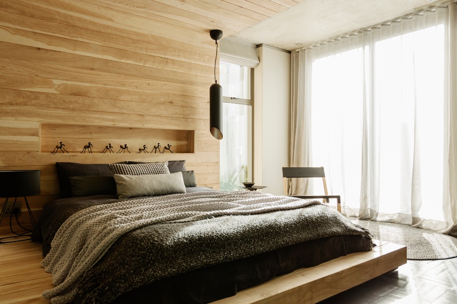 A platform bed built into a wood paneled wall feature. The wall has a cut out shelf with small trinkets on it.