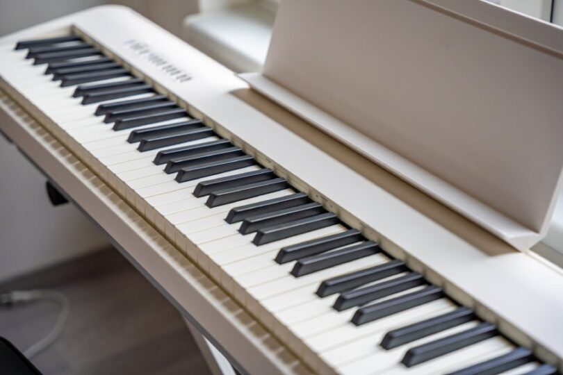 A close-up of a white piano synthesizer with a music tray on its end and sleek white and black keys.