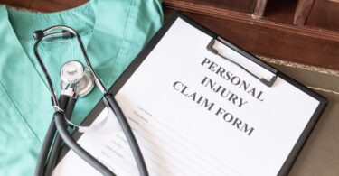 A clipboard holding a Personal Injury Claim Form rests on a desk next to a green medical garment and a stethoscope.