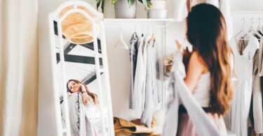 A woman in a pink skirt talks on her mobile phone as she chooses elegant clothes in a bright wardrobe room.