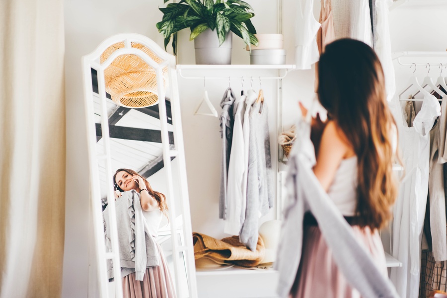 A woman in a pink skirt talks on her mobile phone as she chooses elegant clothes in a bright wardrobe room.