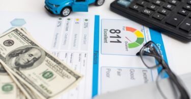 A toy car, a calculator, a pair of glasses, and money sit on a table covering a piece of paper with credit score information.
