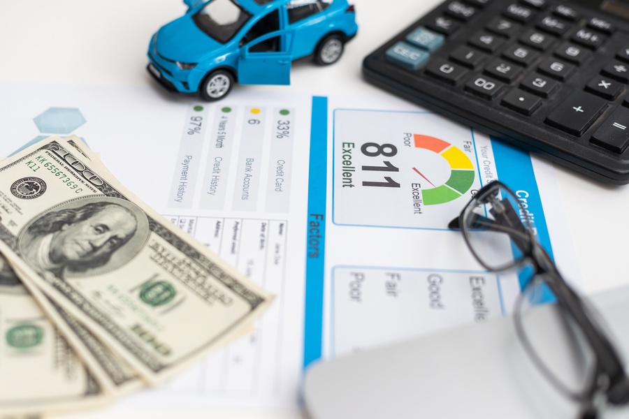 A toy car, a calculator, a pair of glasses, and money sit on a table covering a piece of paper with credit score information.