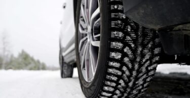 A car driving through a sleek, snowy road. There are snowflakes stuck onto the winter tires of the vehicle.