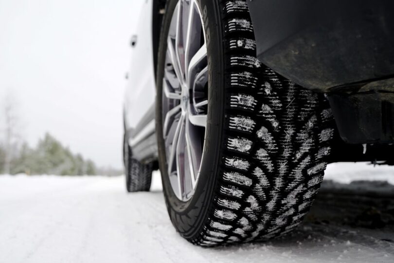 A car driving through a sleek, snowy road. There are snowflakes stuck onto the winter tires of the vehicle.