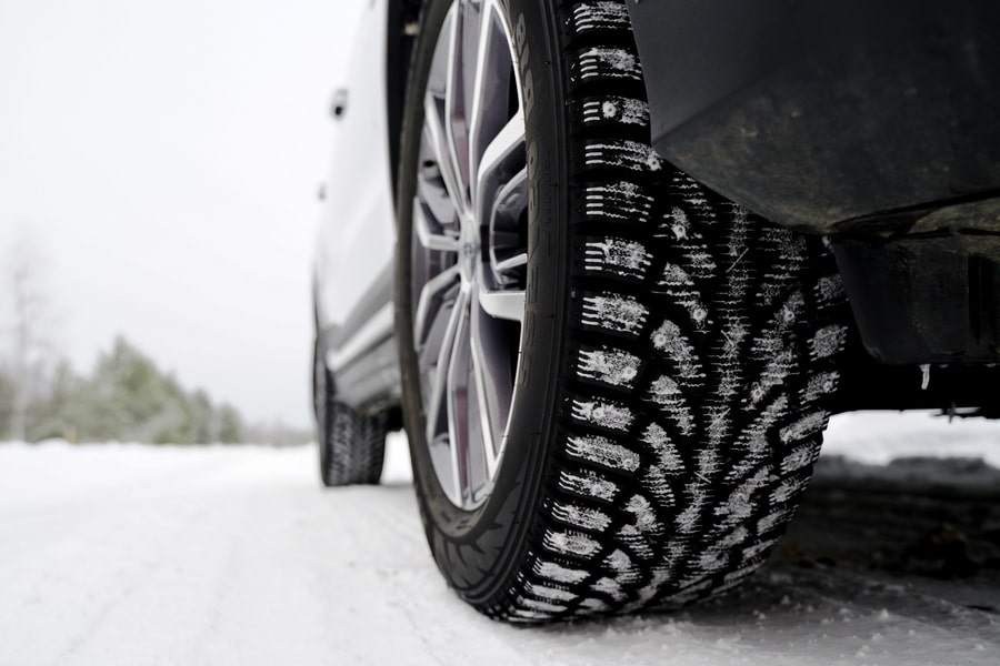 A car driving through a sleek, snowy road. There are snowflakes stuck onto the winter tires of the vehicle.