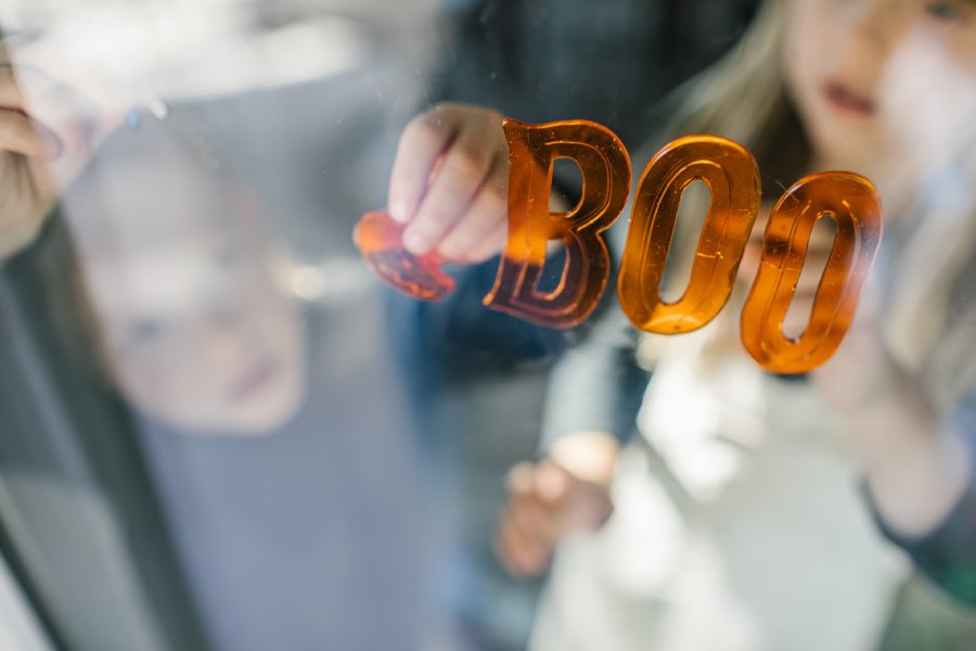 Two children decorate a window with orange stickers that spell the word "boo" and a pumpkin sticker.
